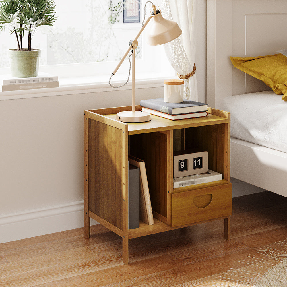 Bamboo side table with open shelf and small drawer beside a bed