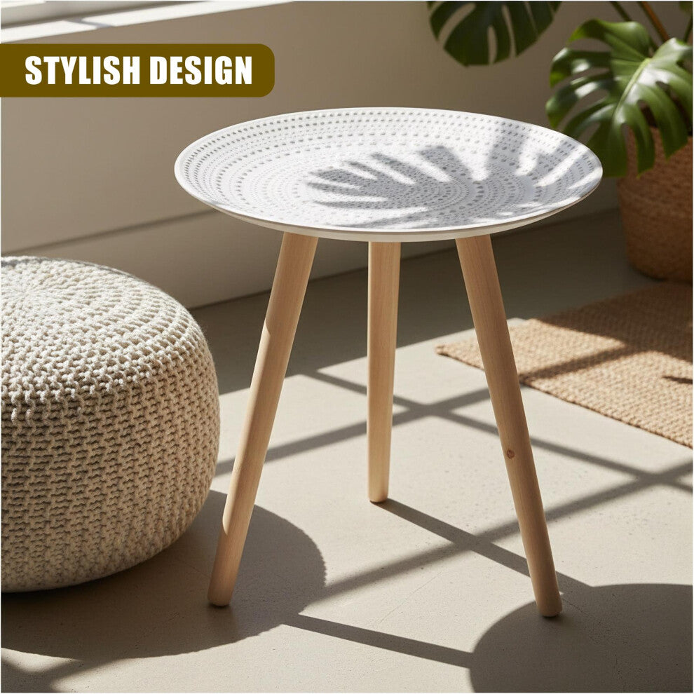 Boho white round side table with three wooden legs beside a knitted pouffe and monstera plant in sunlight