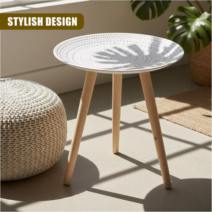 Boho white round side table with three wooden legs beside a knitted pouffe and monstera plant in sunlight