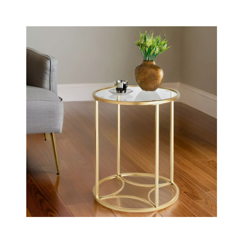 Round gold glass side table with clear top and interlocking arc base beside a grey armchair on a wooden floor