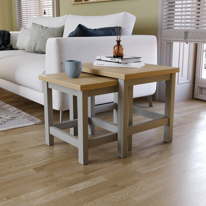 Grey square nest of 2 tables with oak-effect tops beside a white sofa, with a mug, books and reed diffuser