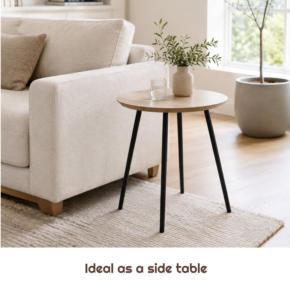 40cm natural wood-effect round end table with splayed black legs next to a sofa arm with a vase of greenery