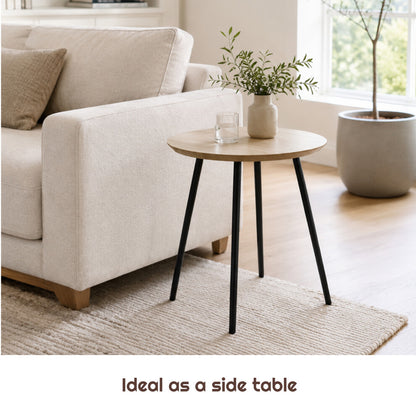 40cm natural wood-effect round end table with splayed black legs next to a sofa arm with a vase of greenery