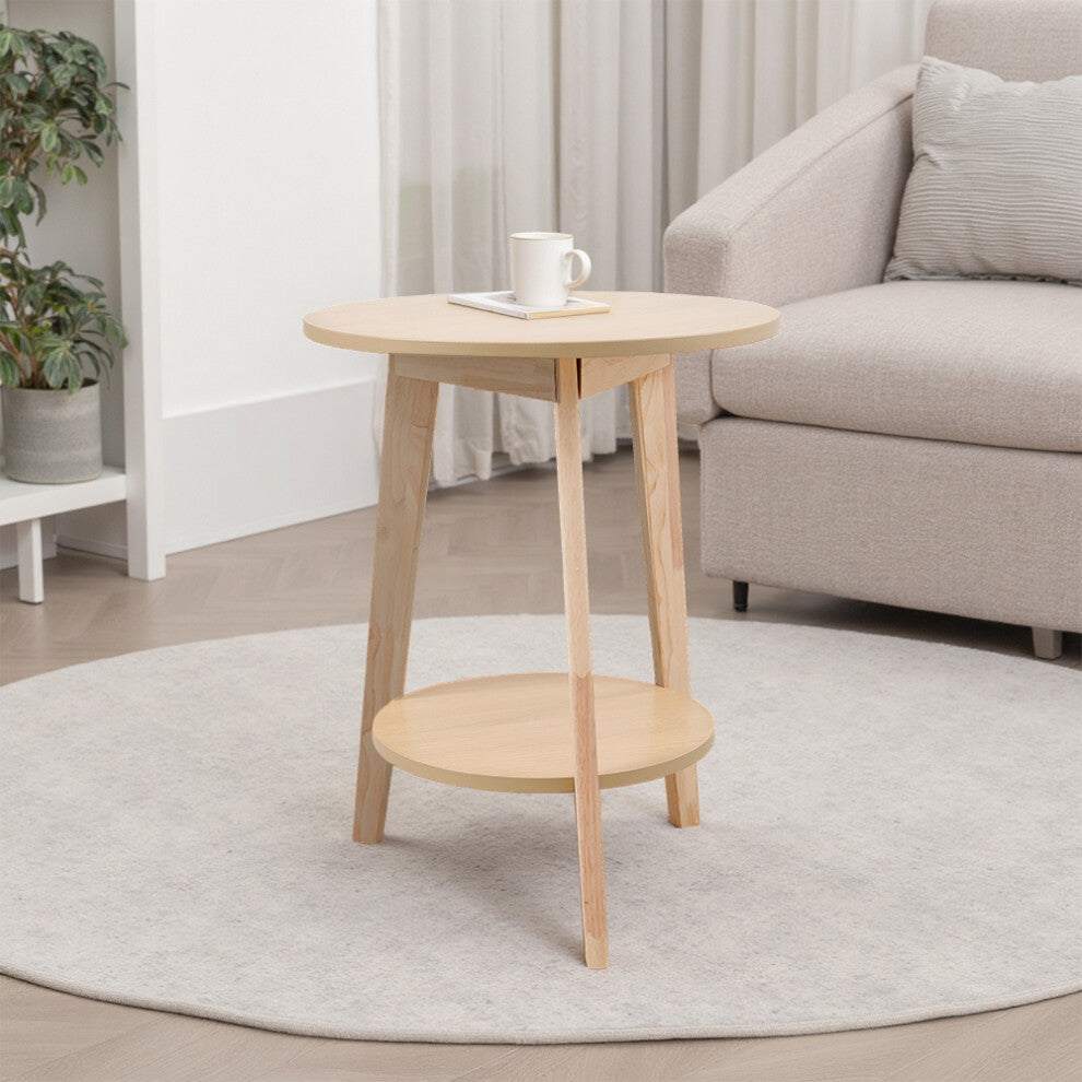 Natural wood round end table with lower shelf and three solid wood legs beside a beige armchair