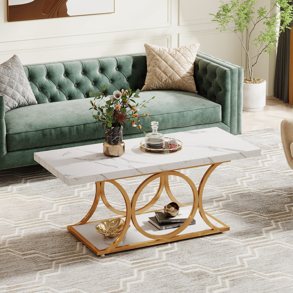 Rectangular white faux marble coffee table with gold ring base and lower shelf beside a green velvet sofa