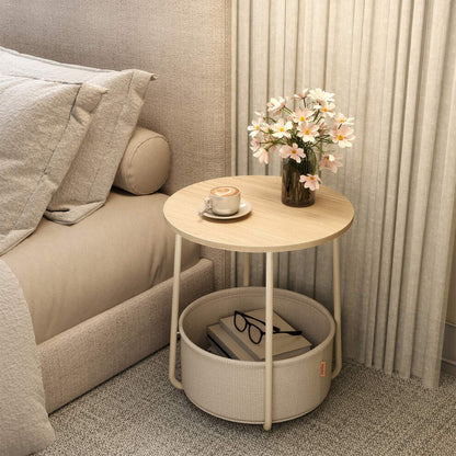 Round side table with fabric basket used as a bedside table with coffee and pink flowers