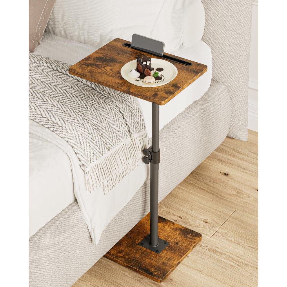 Rustic brown height adjustable side table next to a bed holding a phone and a dessert plate
