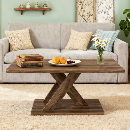 Rustic brown woodgrain coffee table with crossed pedestal legs in front of a grey sofa