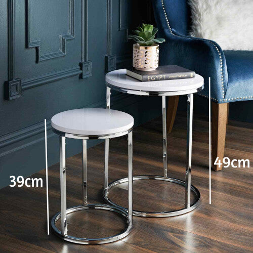 Set of 2 round side tables with glossy white tops and chrome frames, 49cm and 39cm high, beside a blue velvet armchair