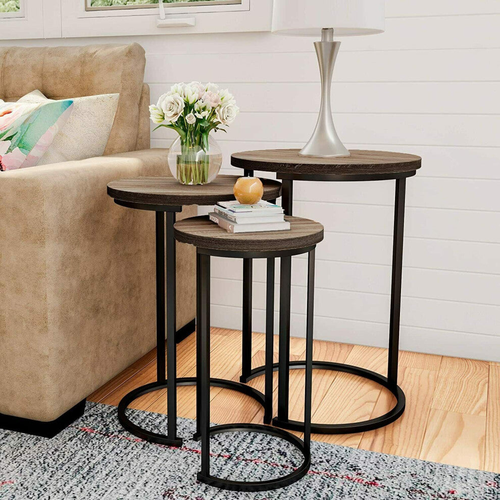 Set of 3 round side tables staggered beside a beige sofa with flowers and books