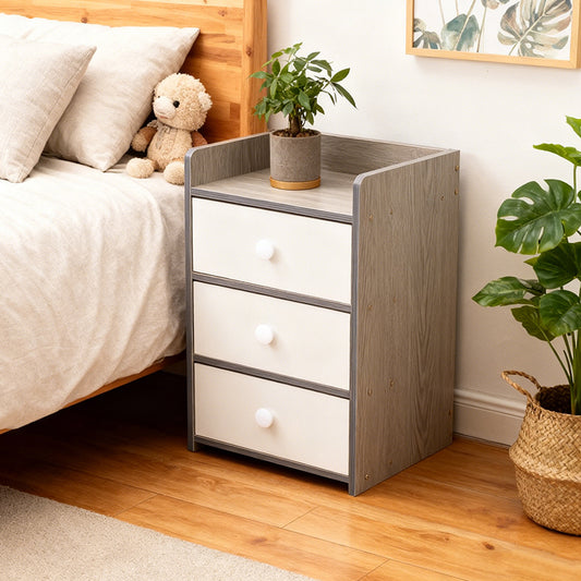 Small bedside cabinet with three drawers beside a wooden bed and green plant