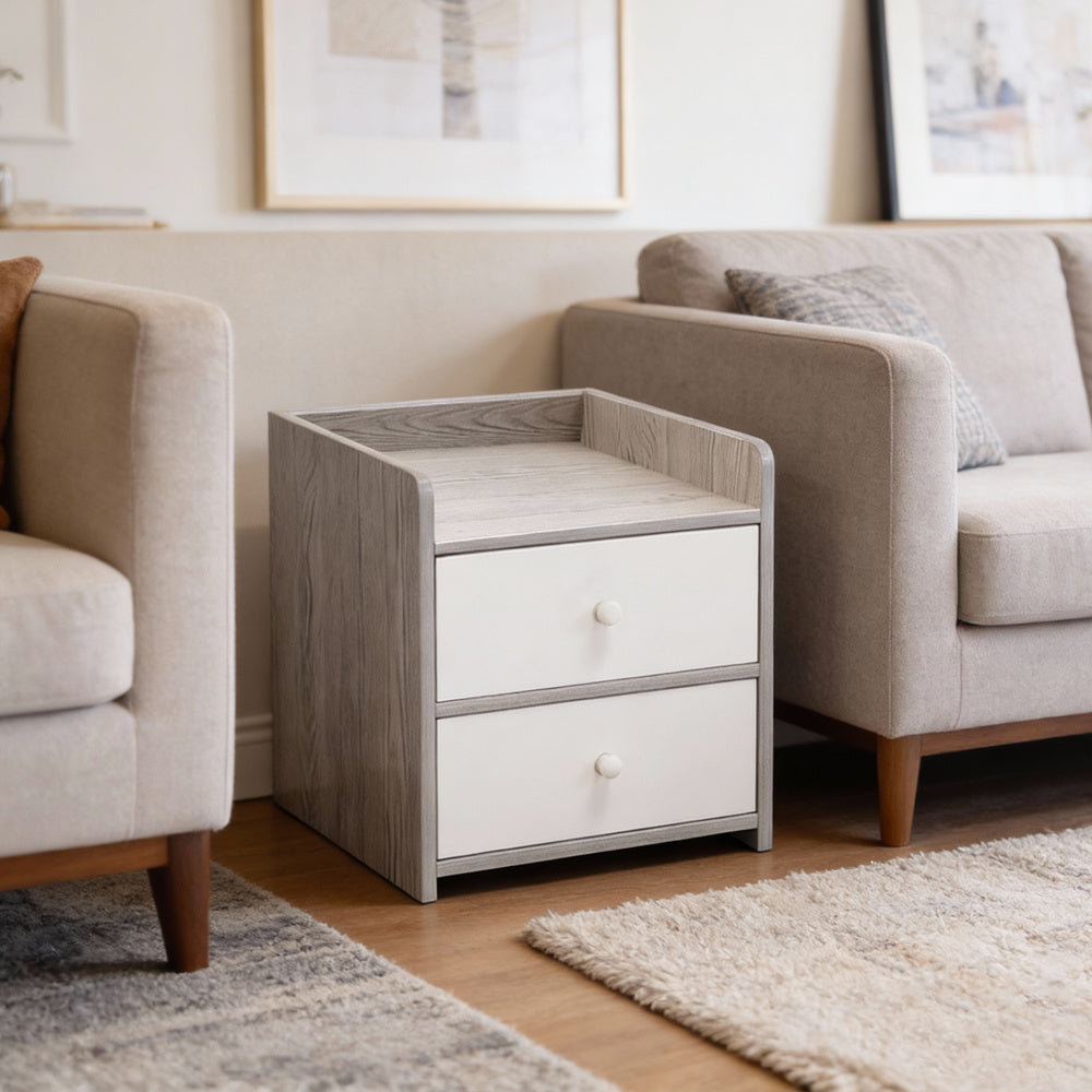 Small grey and white two-drawer side table beside a beige sofa