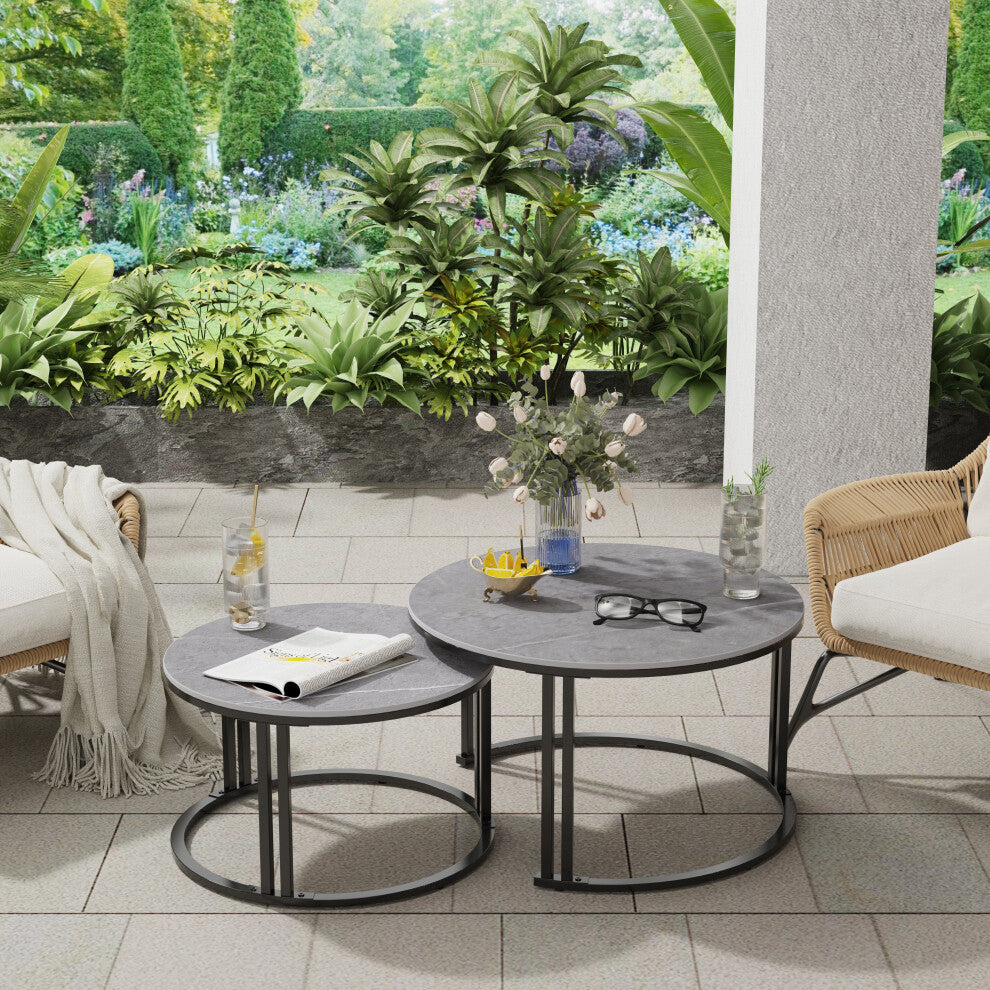 Two round coffee tables with grey tops and black frames styled with rattan chairs and plants