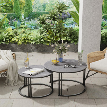 Two round coffee tables with grey tops and black frames styled with rattan chairs and plants