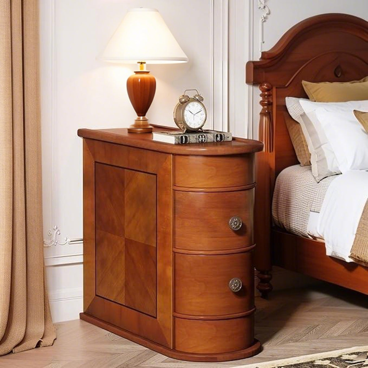 Walnut side table with two curved drawers beside a bed with a table lamp and alarm clock