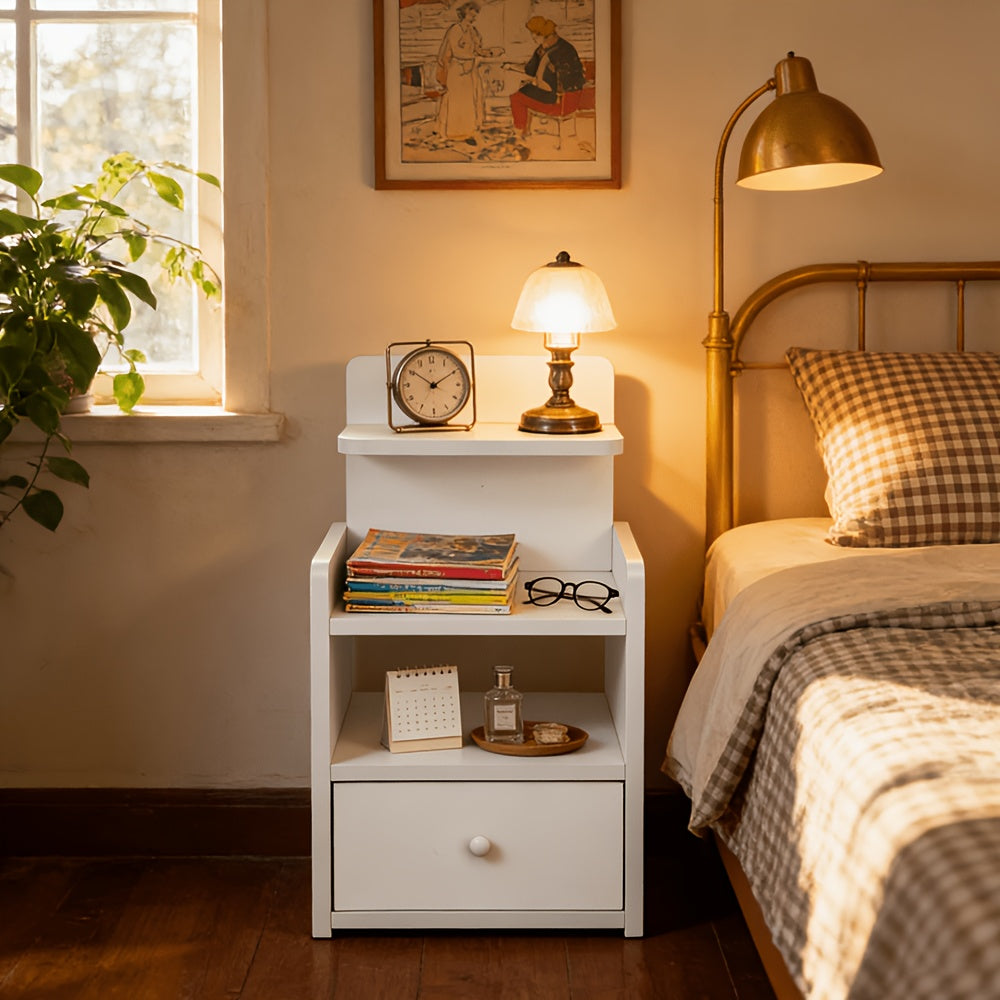 White nightstand with drawer and open shelf beside a brass-framed bed and lamp