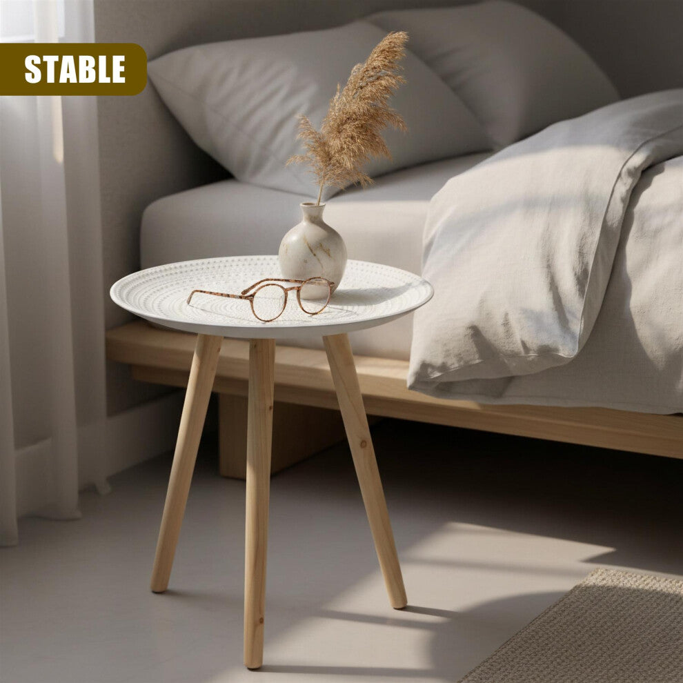 White round tray side table with embossed dot top and natural wood tripod legs used as a bedside table with a vase and glasses