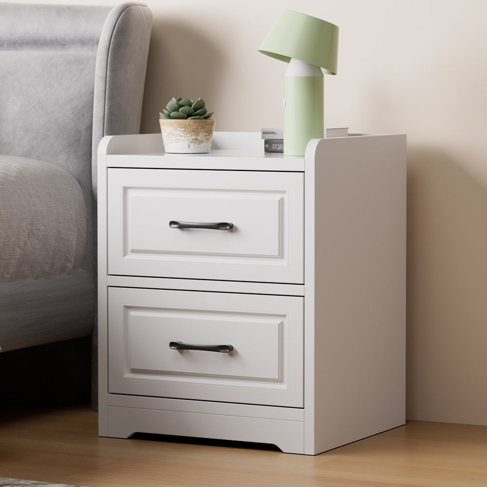 White side table with two storage drawers and black handles beside a bed