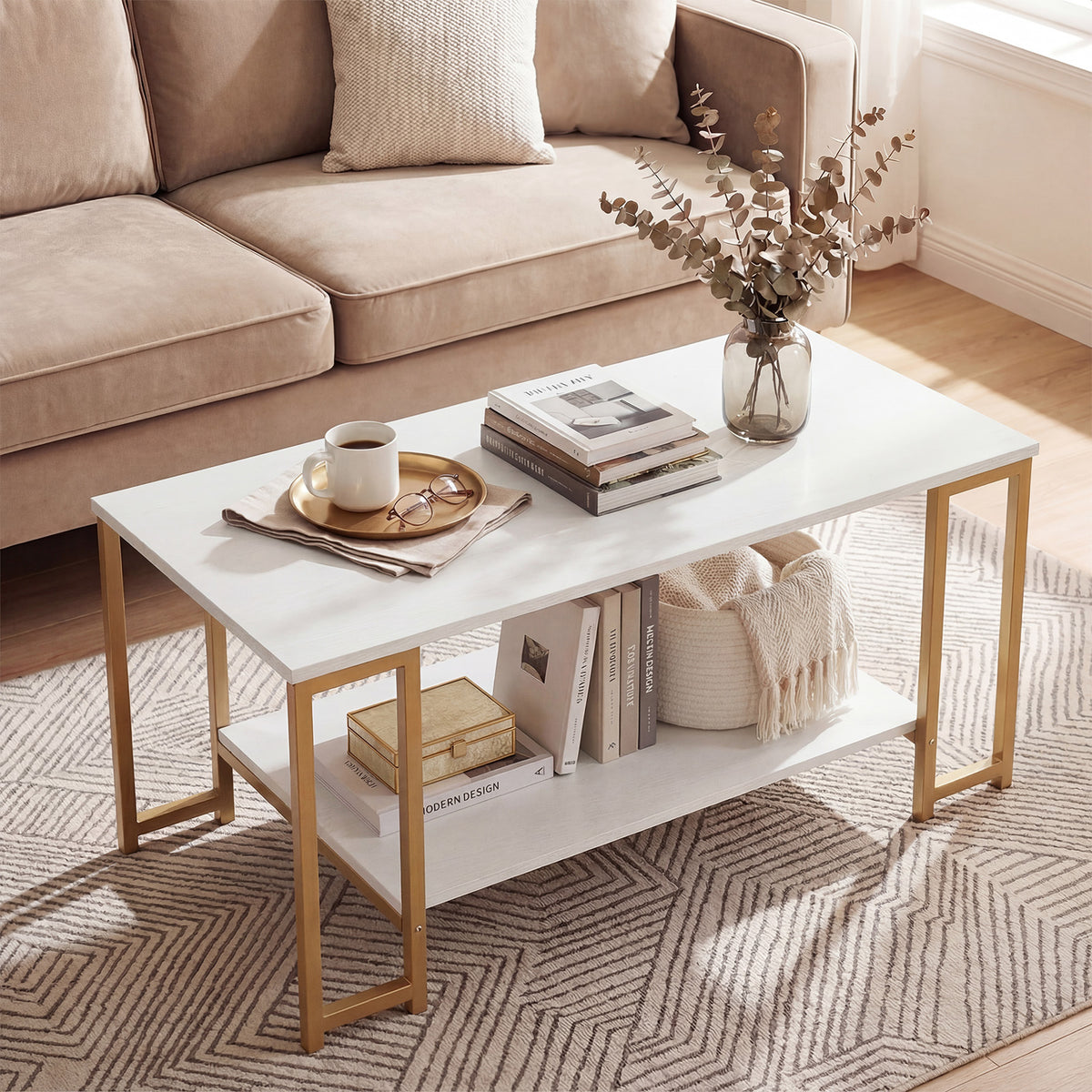 White two-tier coffee table with gold-tone metal legs styled with tea tray, books and vase